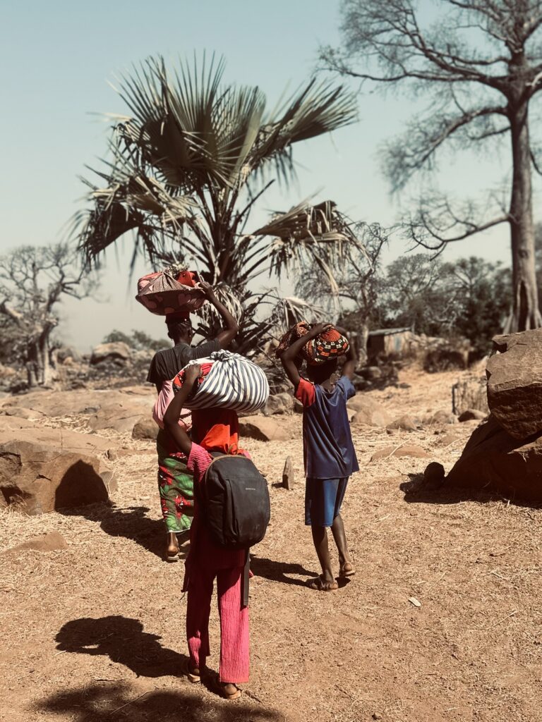 Mujeres con los niños a cuestas y los productos en la cabeza